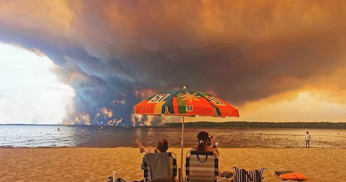 Unos bañistas observan hacia el sur desde la playa de Moutchic, en Lacanau, al suroeste de Francia, mientras las nubes de humo del incendio forestal de Gironda se elevan hacia el cielo. [Getty Images]