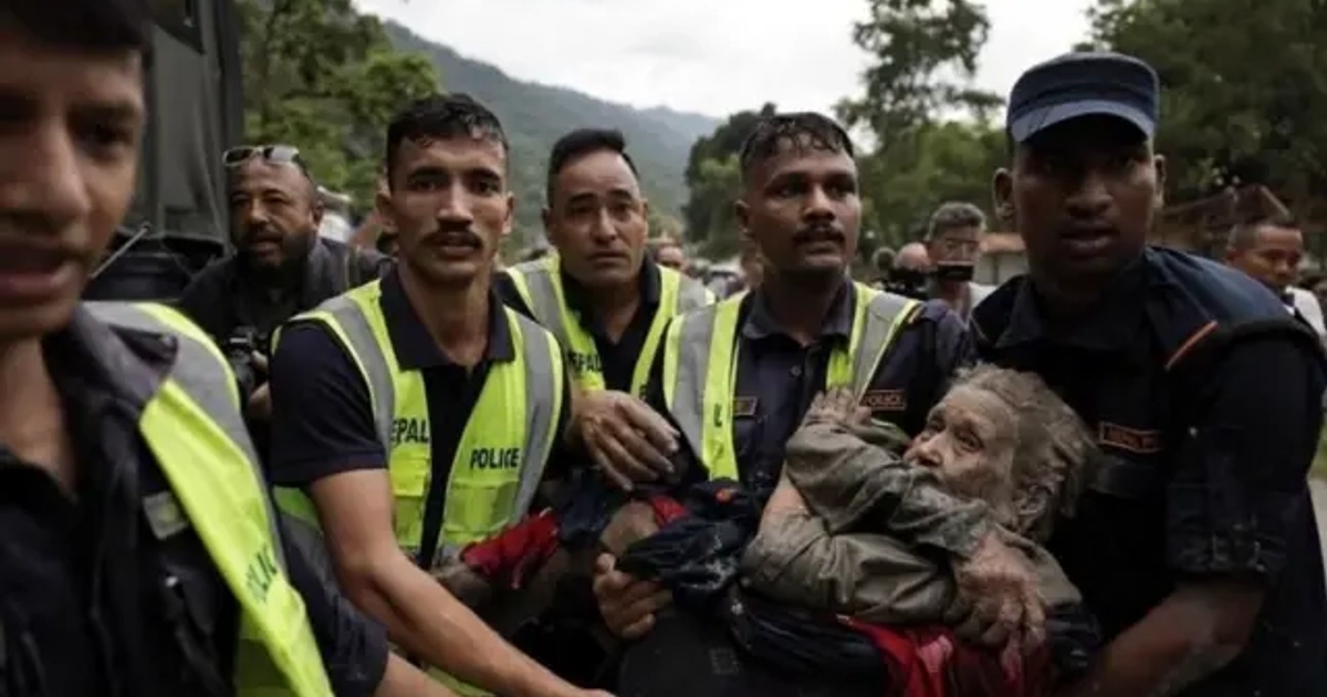 Un hombre cubierto de lodo es llevado por cinco hombres que visten chalecos reflectantes.