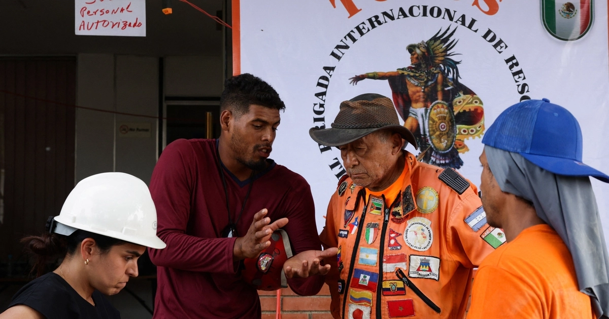 Héctor Méndez, conocido como 'el Chino', de 78 años, presidente y fundador del grupo internacional de rescatistas mexicanos, conversa con rescatistas mientras la gente busca entre los escombros tras los terremotos del 24 de junio, en La Guaira, Venezuela, el 10 de julio de 2026. REUTERS/Gaby Oraa