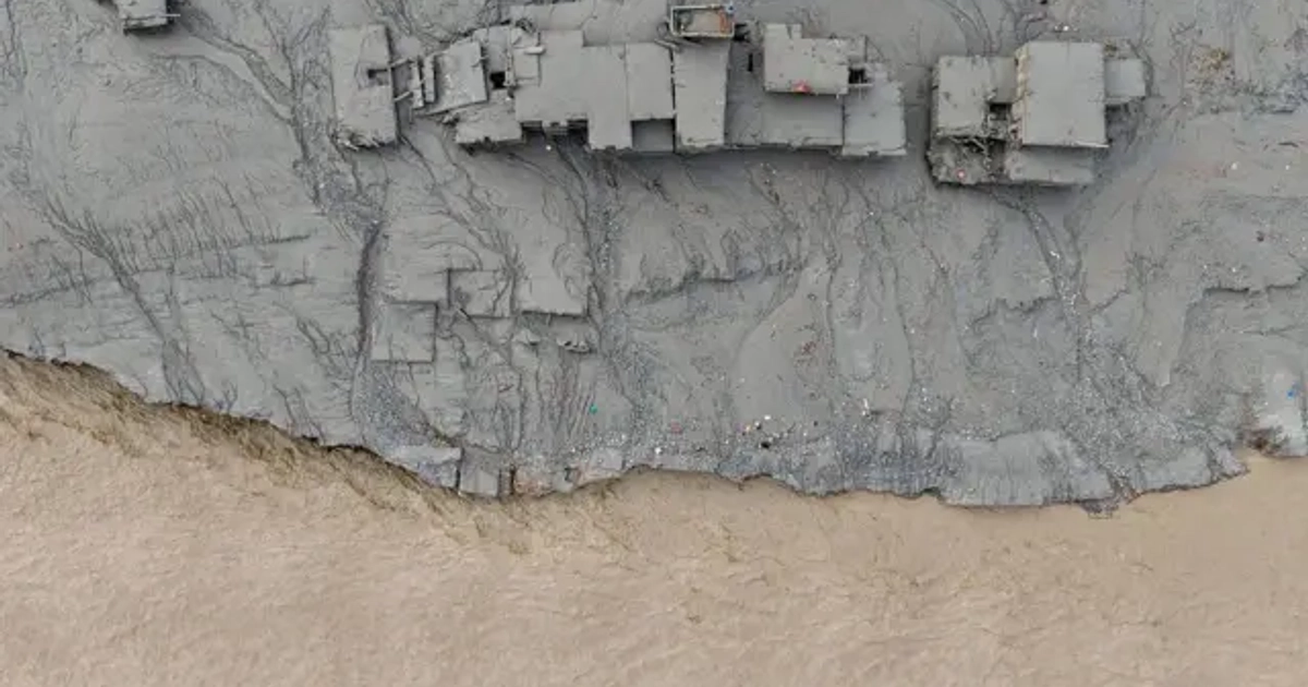 Un río marrón pasa al lado de una serie de construcciones cubiertas de barro debido a una avalancha reciente. La foto es tomada desde arriba.