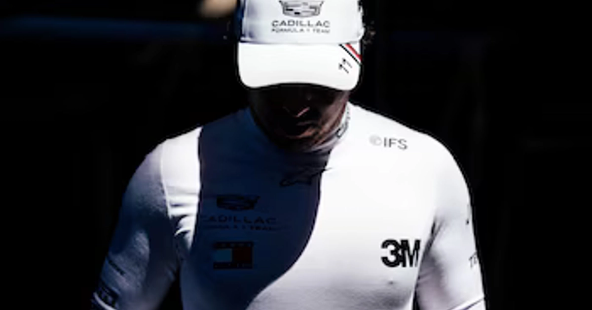 Un piloto con gorra y prenda blanca que exhiben el logotipo de Cadillac Formula 1 Team, el número once y otras marcas.