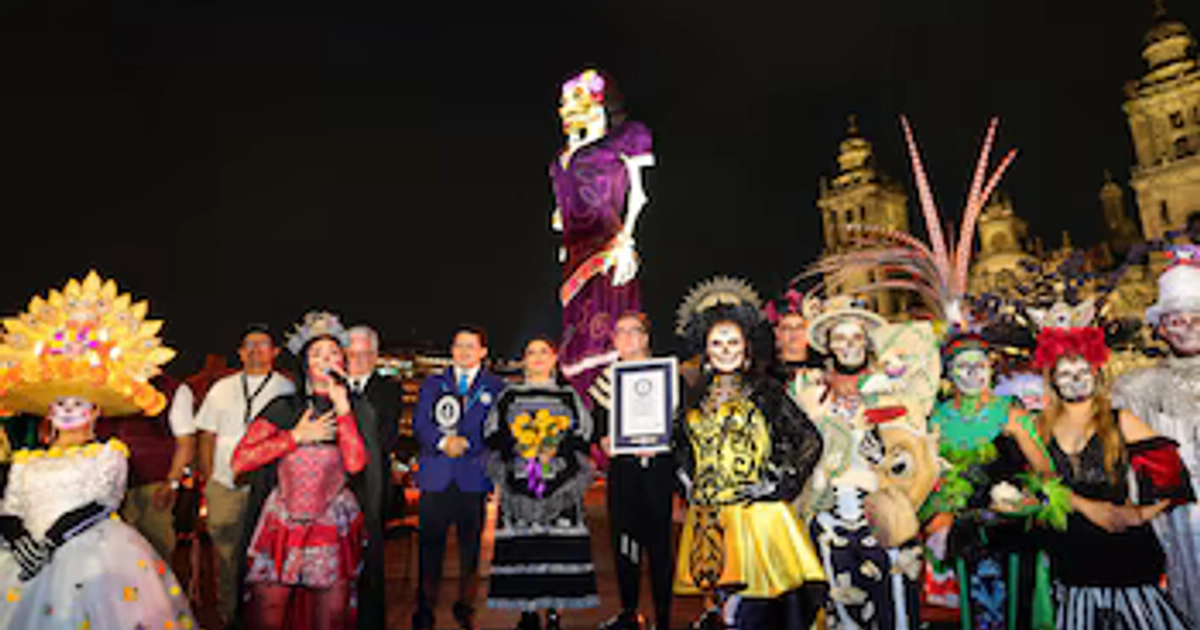 Autoridades de la CDMX y participantes caracterizados presentan un reconocimiento frente a una catrina monumental durante la inauguración de la ofrenda en el Zócalo de la Ciudad de México. (Gobierno CDMX)