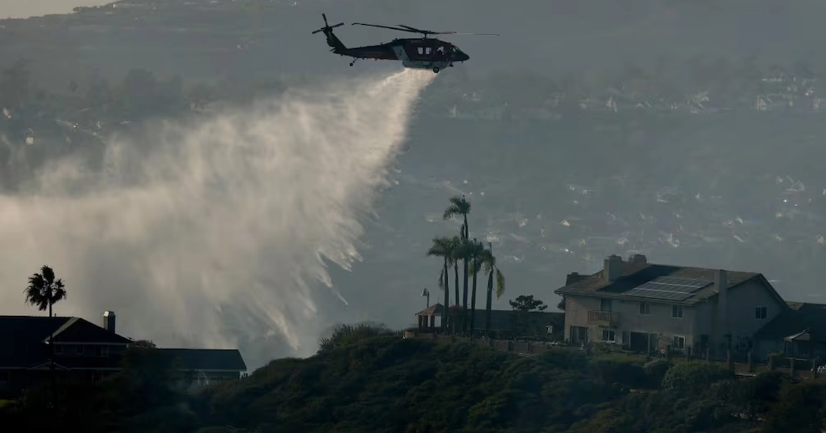Un helicóptero de extinción de incendios arroja agua sobre el incendio Norte este 16 de octubre de 2026 en San Juan Capistrano, California. Foto: Justin Sullivan/AFP