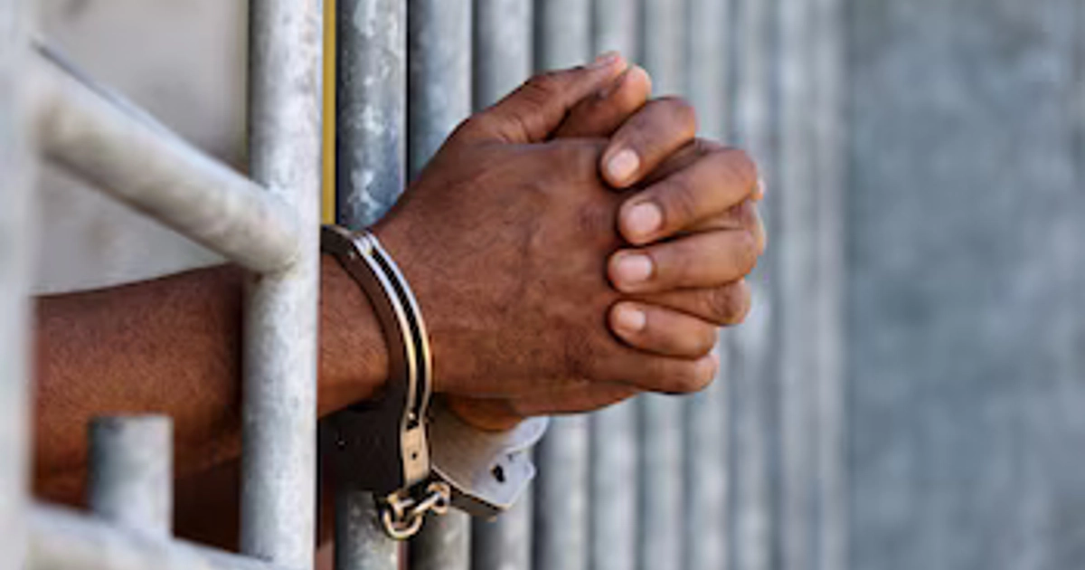 Las manos de una persona detenida permanecen entrelazadas y sujetas por esposas metálicas tras los barrotes de una celda. (Imagen Ilustrativa Infobae)