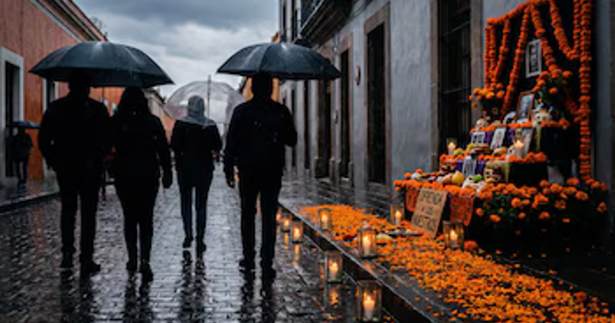 Cuatro personas caminan de espaldas con paraguas por una calle mojada junto a una banqueta con faroles y un altar con flores anaranjadas.