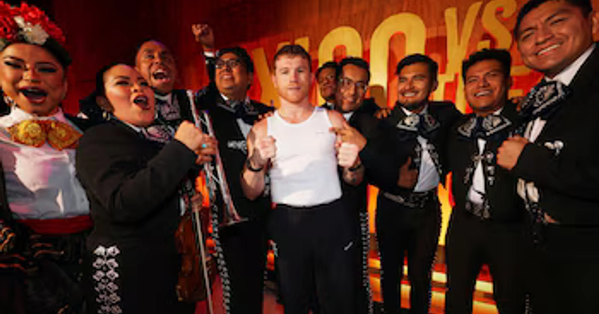Saúl Canelo Álvarez en camiseta blanca junto a varios músicos de mariachi con trajes negros e instrumentos musicales frente a un panel.