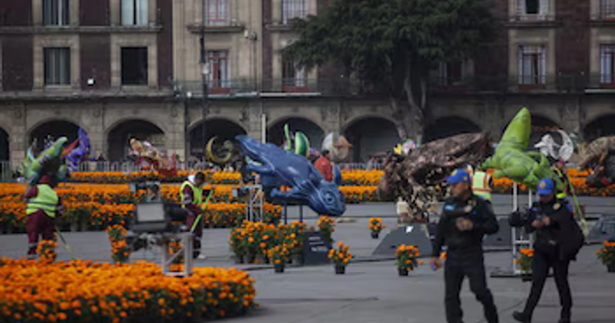 Trabajadores y policías recorren la explanada del Zócalo de Ciudad de México entre figuras monumentales y flores de cempasúchil antes de la apertura al público. (ANDREA MURCIA /CUARTOSCURO.COM)