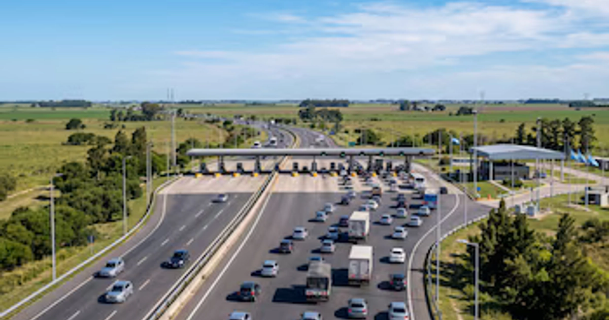 Una autopista de varios carriles con automóviles y camiones que se aproximan a una estación de peaje en una zona rural