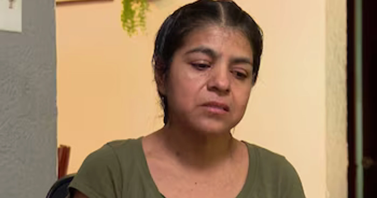 Una mujer con el cabello oscuro y camiseta verde mira hacia abajo en un espacio interior
